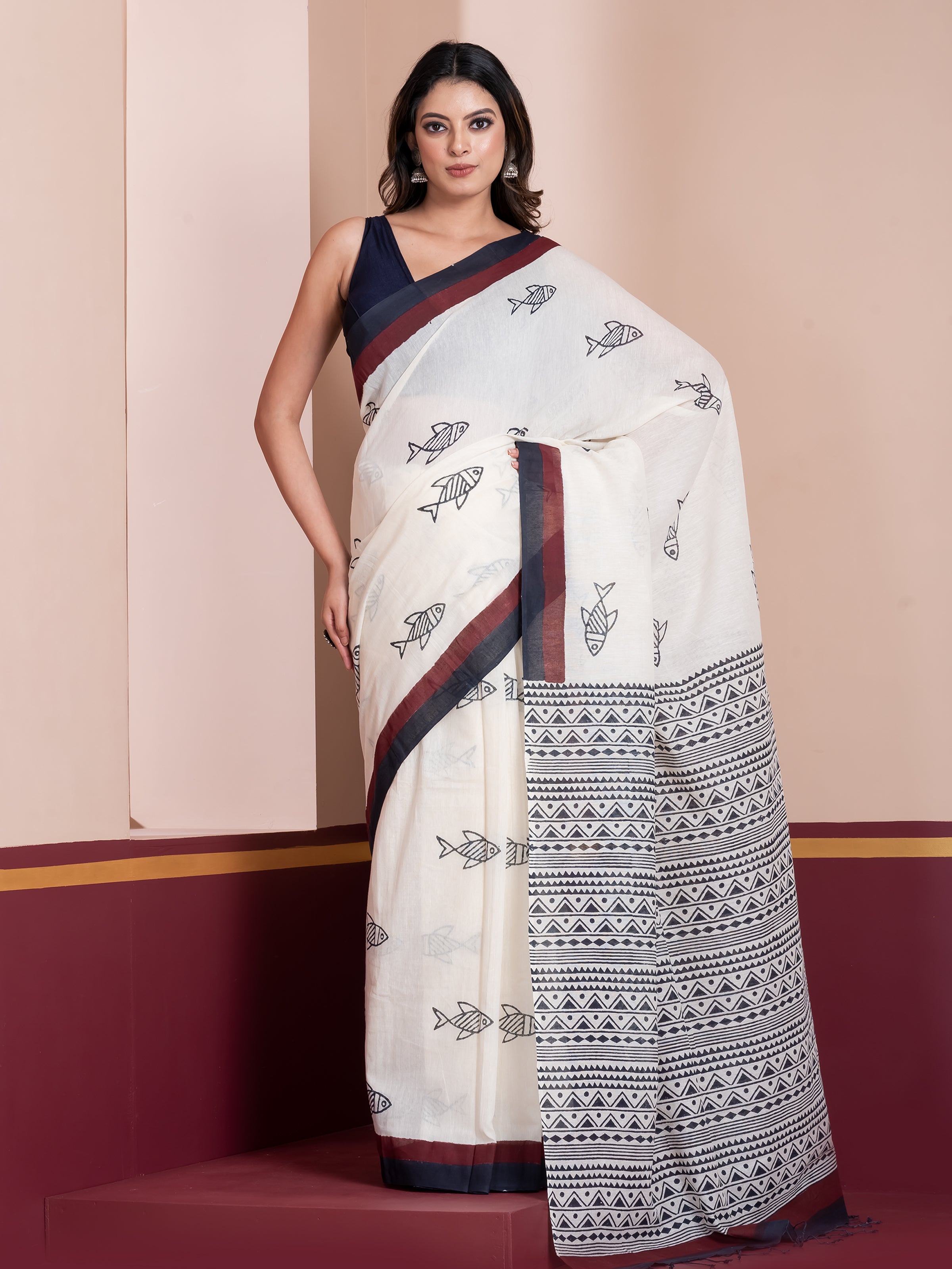 A woman modeling an off-white khadi cotton saree with black and maroon handblock print and borders.