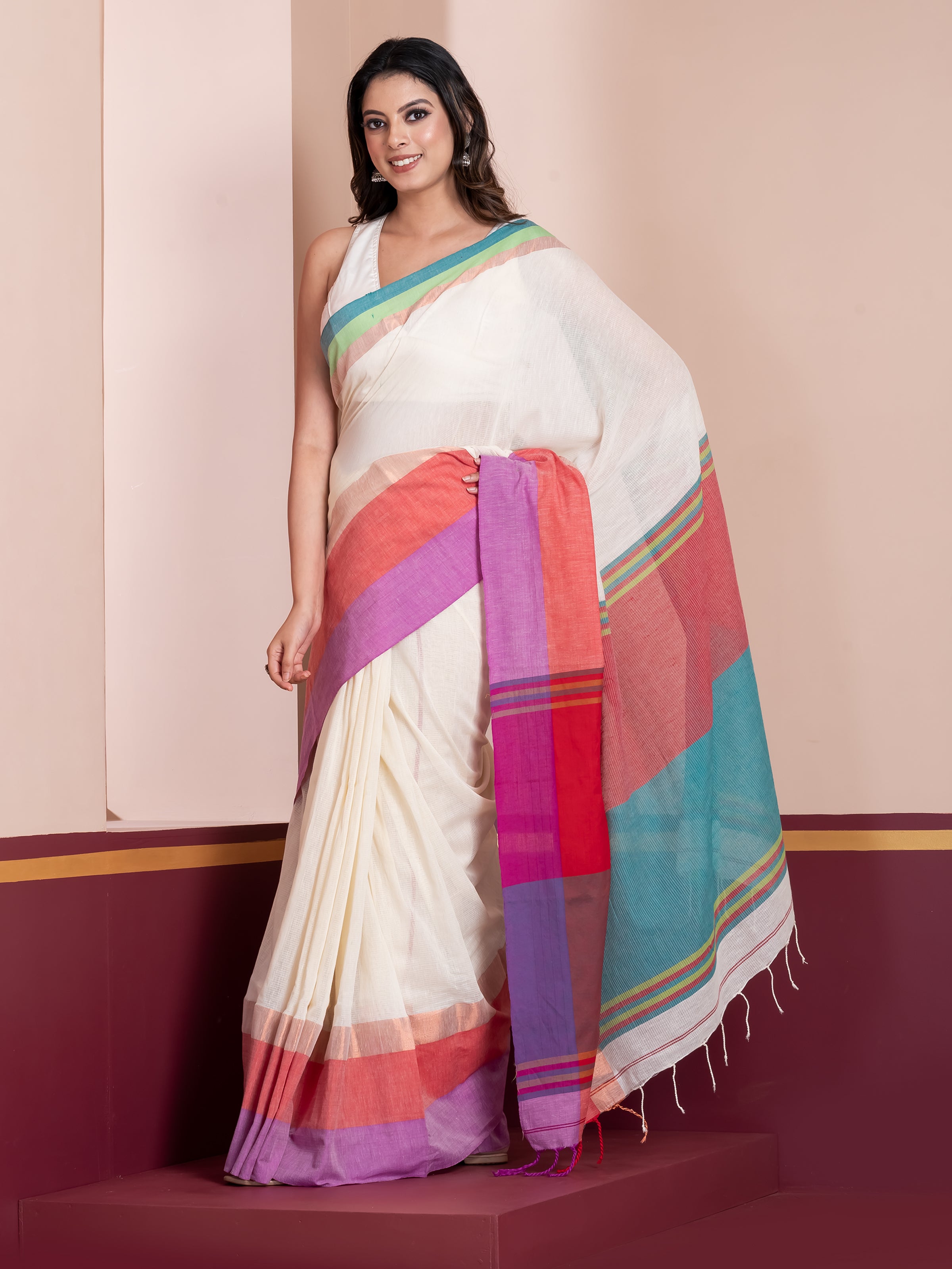 A woman modeling a white khaadi cotton saree with multicolored stripes and borders, standing against a plain background.