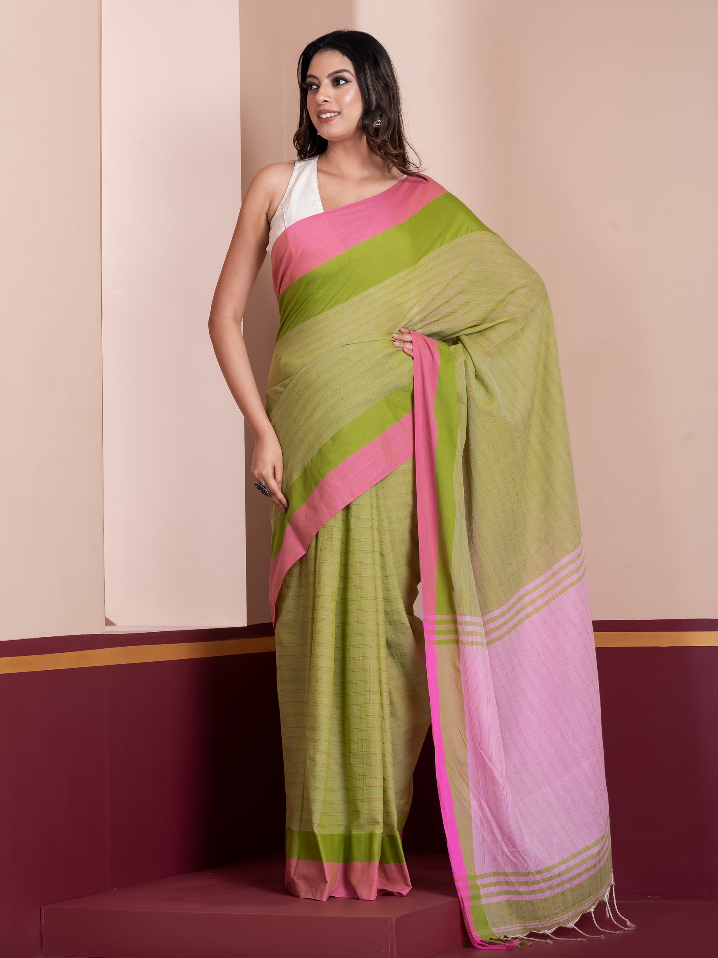 A woman modeling a khadi cotton saree with a green body and pink borders, with additional details such as a white blouse and pompom finishing at the aanchal end.