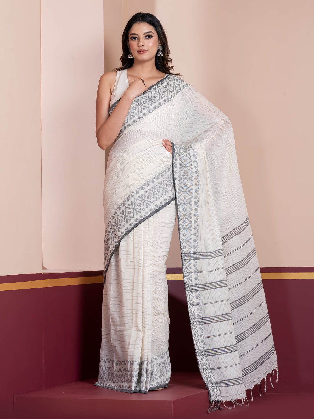 A woman modeling a white khadi cotton saree with a striped pattern and Jamdani border.