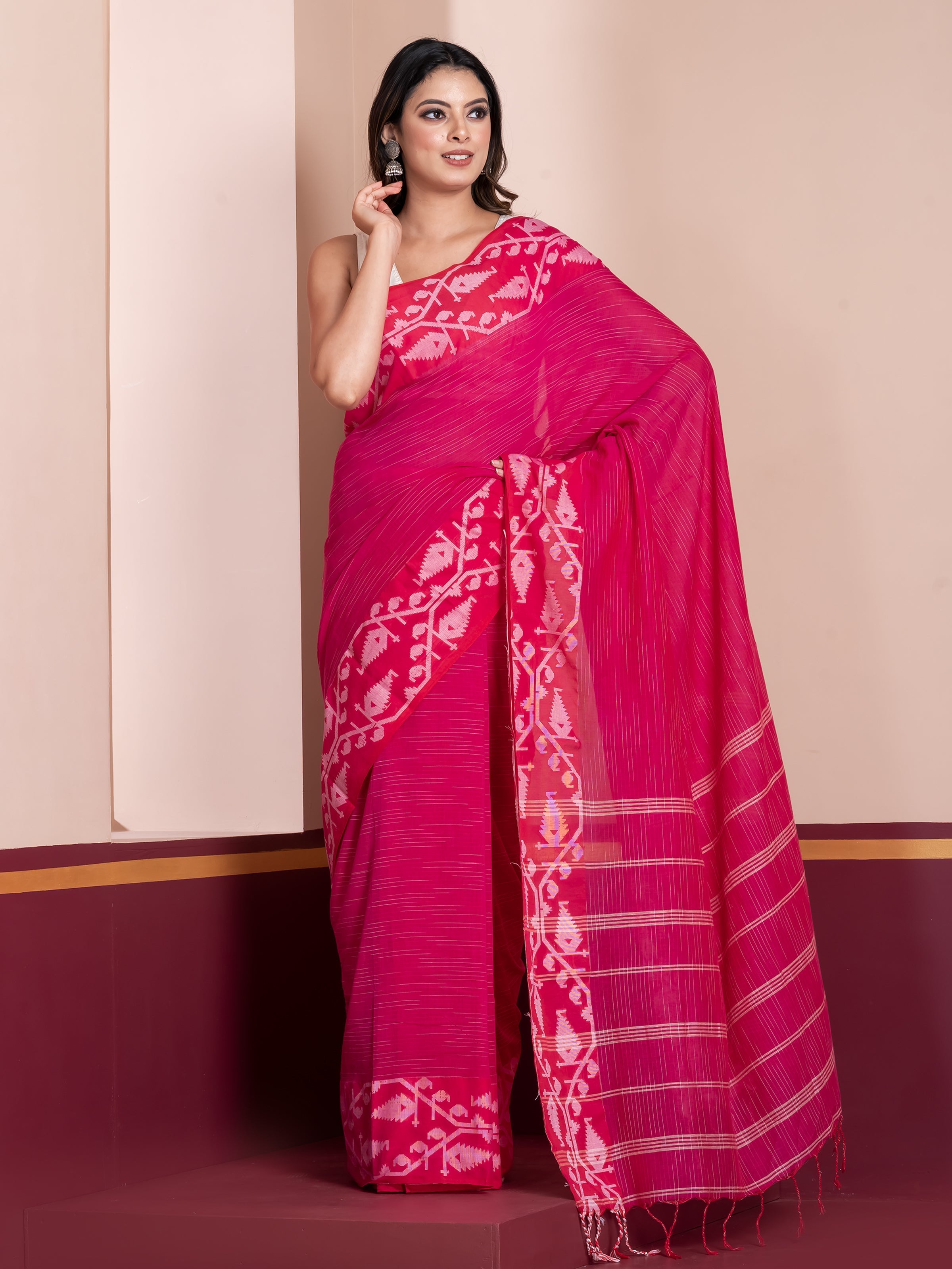A woman modeling a dark pink saree with white border and geometric patterns.