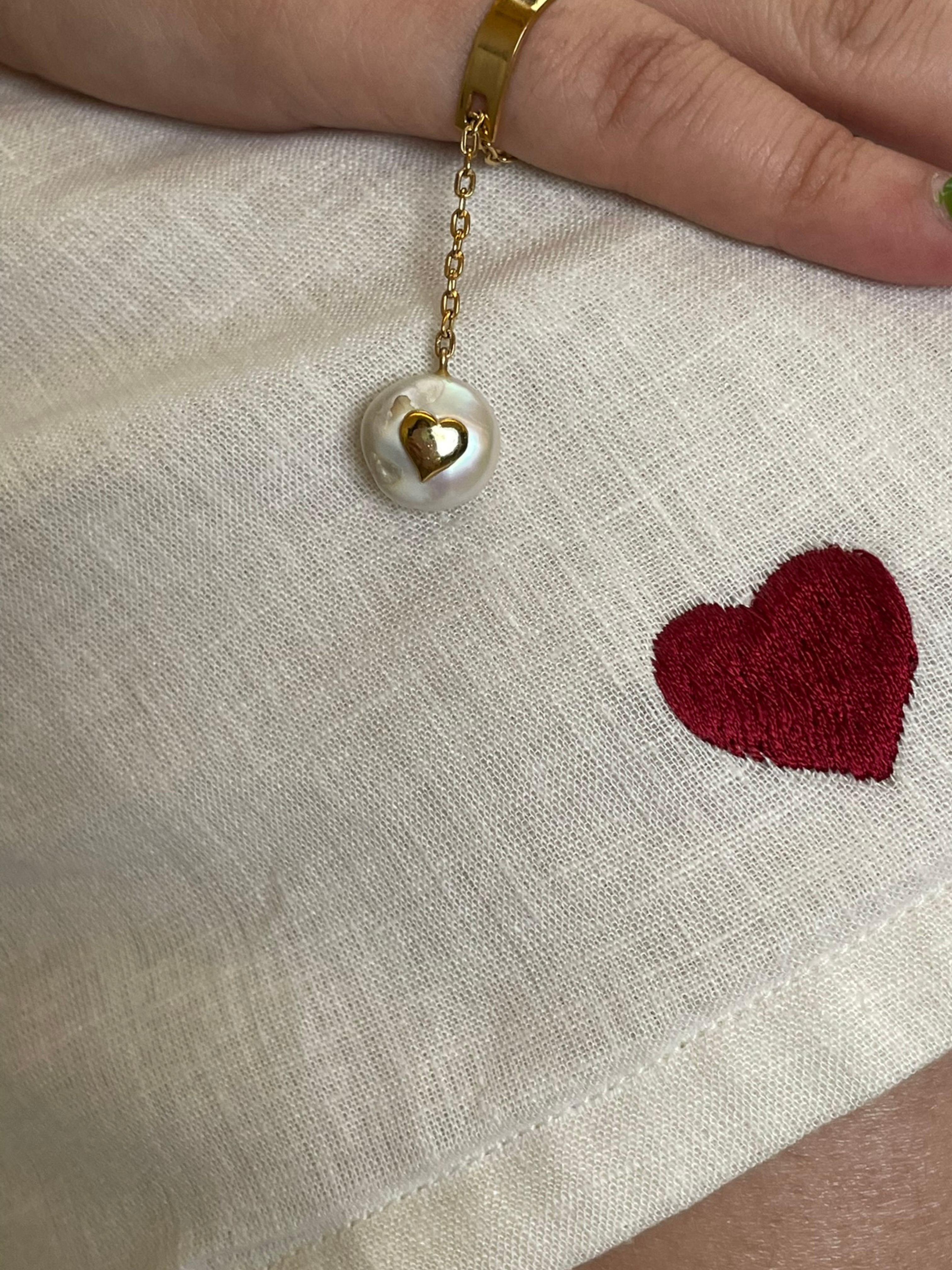 Hand with gold bracelet on white fabric with red heart embroidery