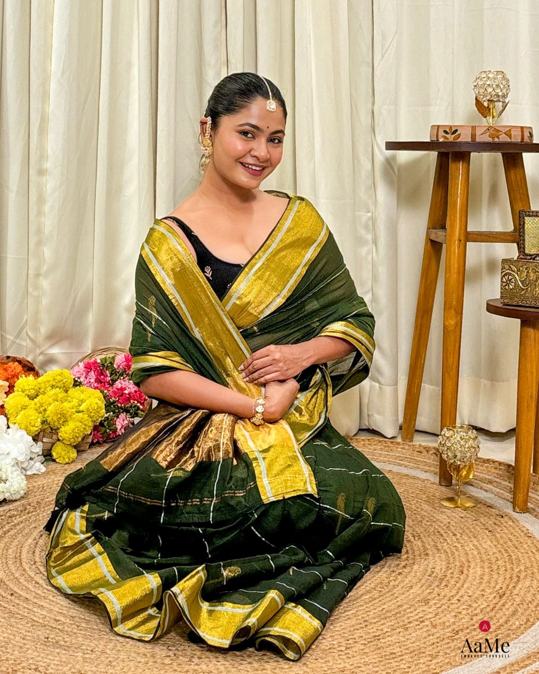 Woman in a handcrafted green mulmul cotton saree sitting on the floor with flowers