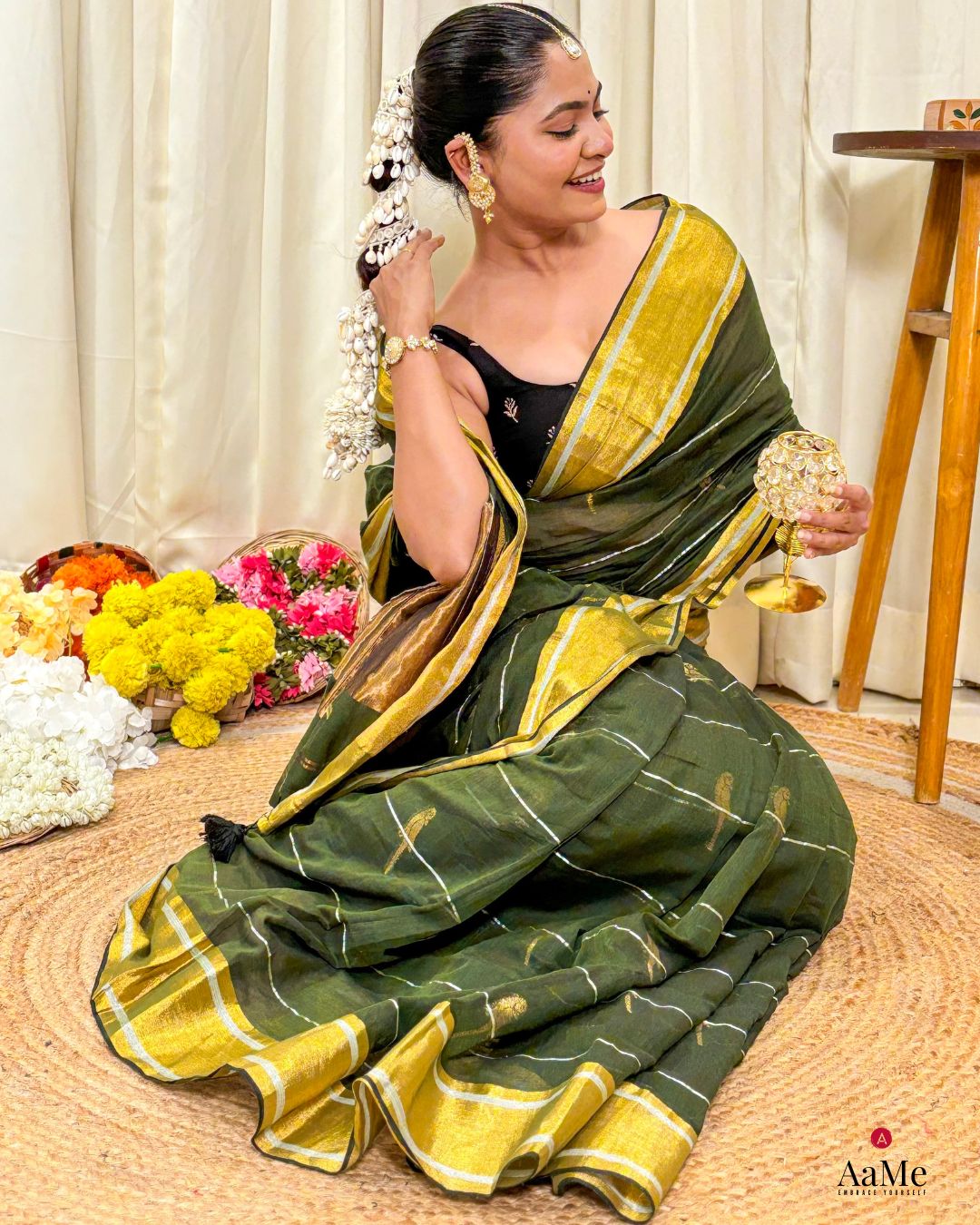 Woman in a handcrafted green mulmul cotton saree sitting on the floor with flowers