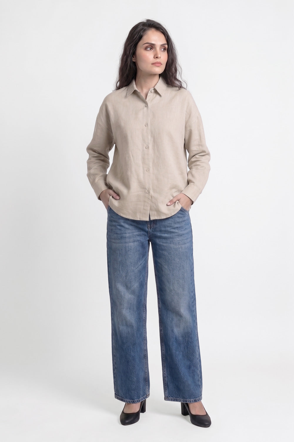 A woman modeling a light beige linen button-up shirt and wide-leg blue jeans against a plain white studio background.