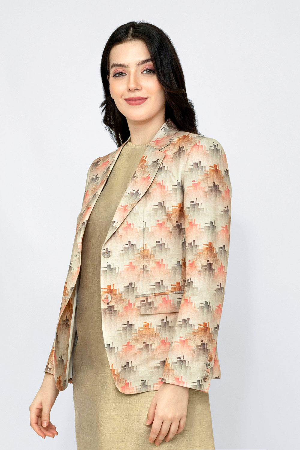 A woman modeling a beige linen blazer with a geometric pattern in orange, pink, and gray, worn over a solid beige dress against a light gray studio background.