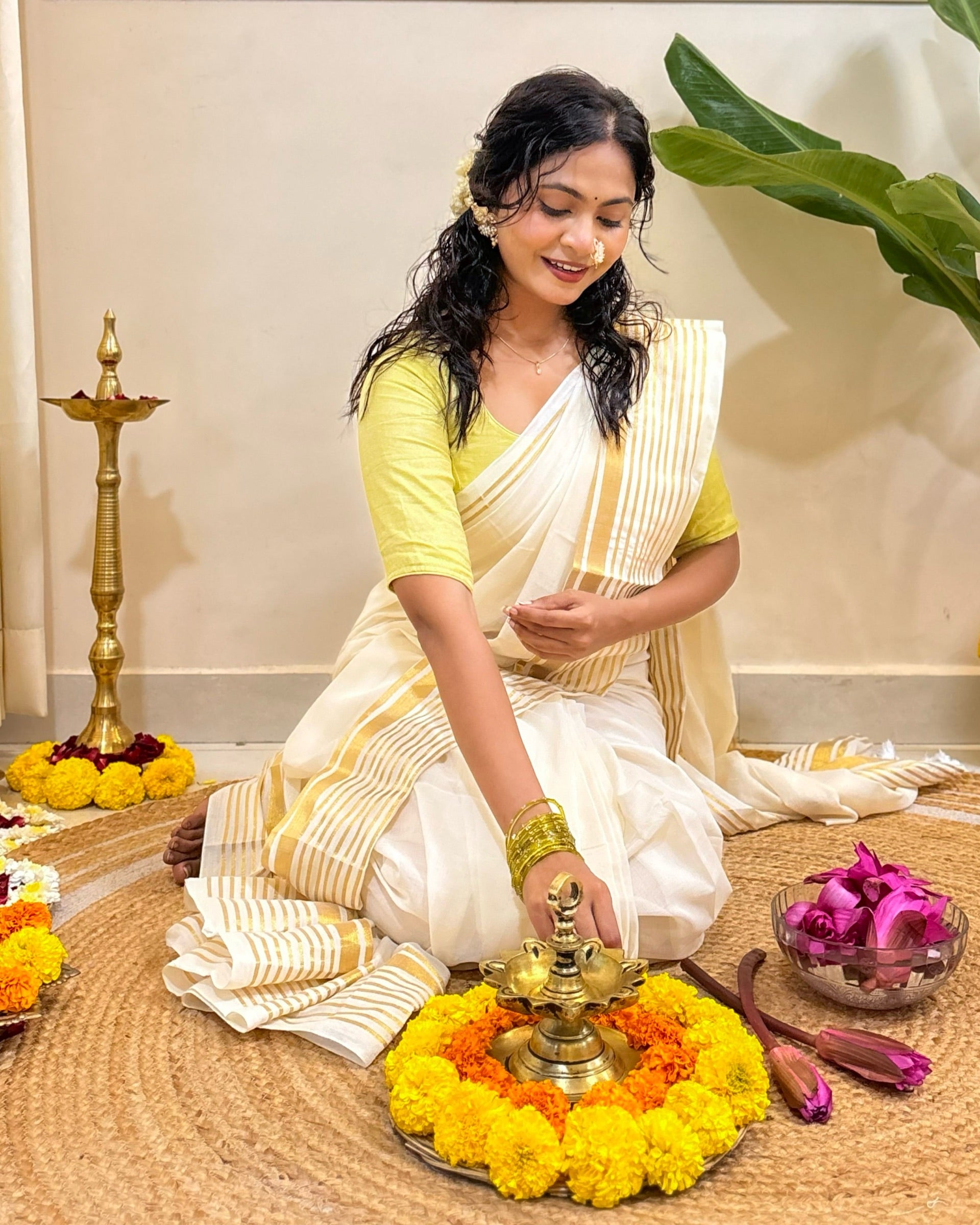 Woman in traditional white mulmul cotton saree performing a ritual with marigold flowers and other offerings.