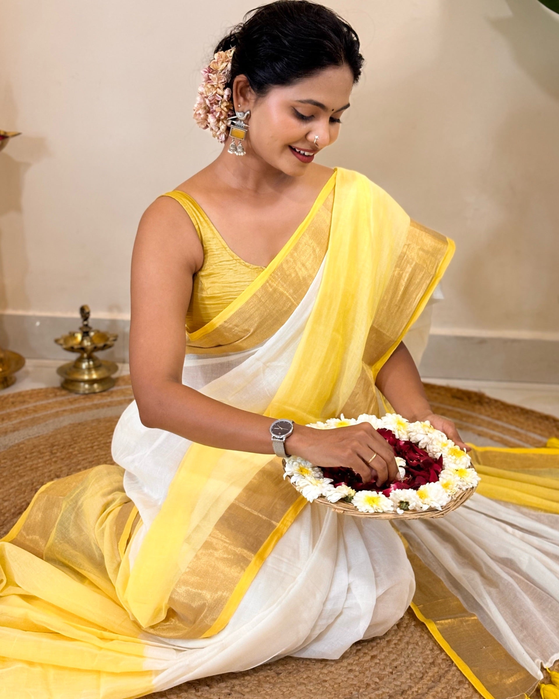 Woman in a yellow and white saree holding a floral offering.
