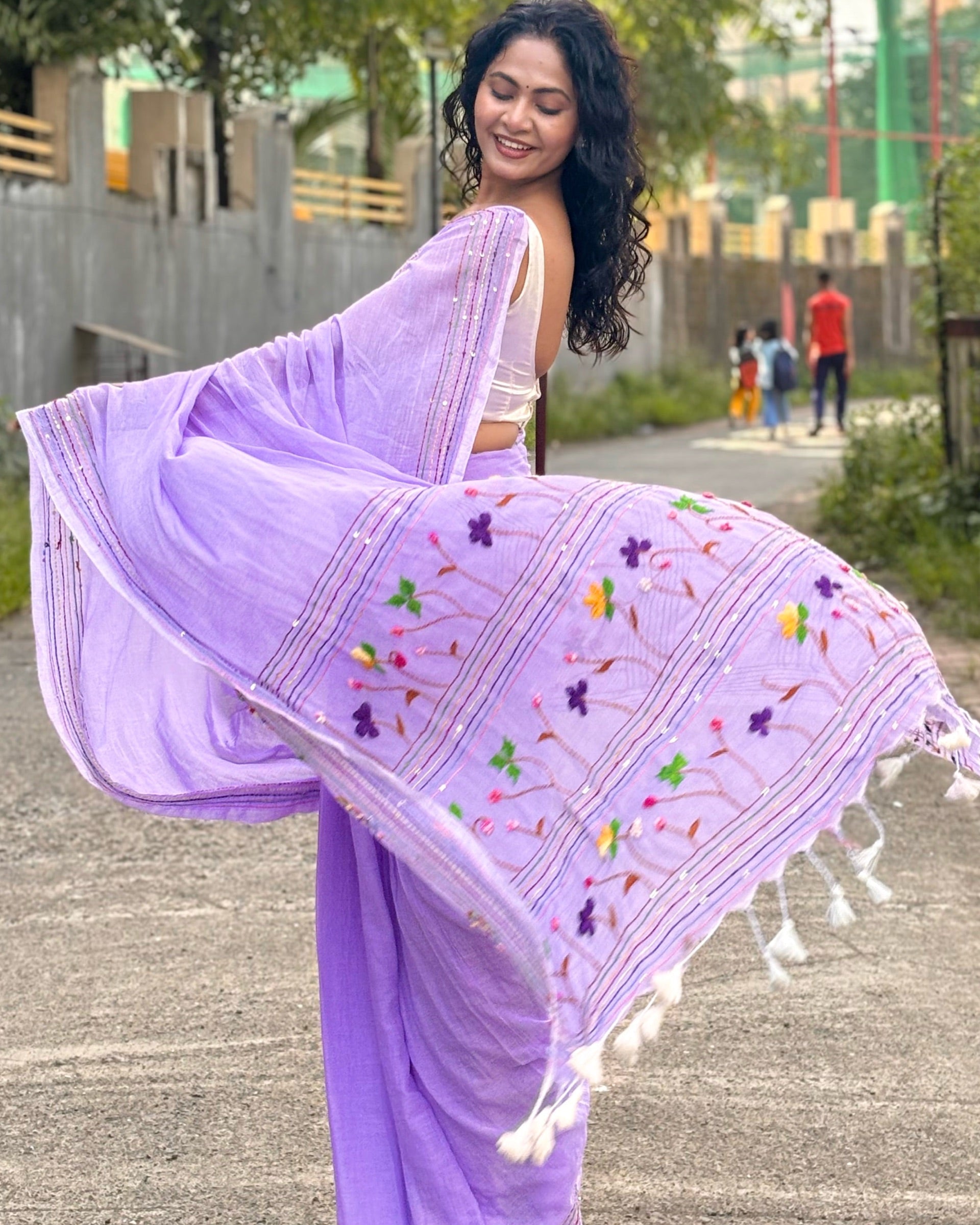 Woman in a mauve mulmul cotton saree with floral embroidery walking outdoors.