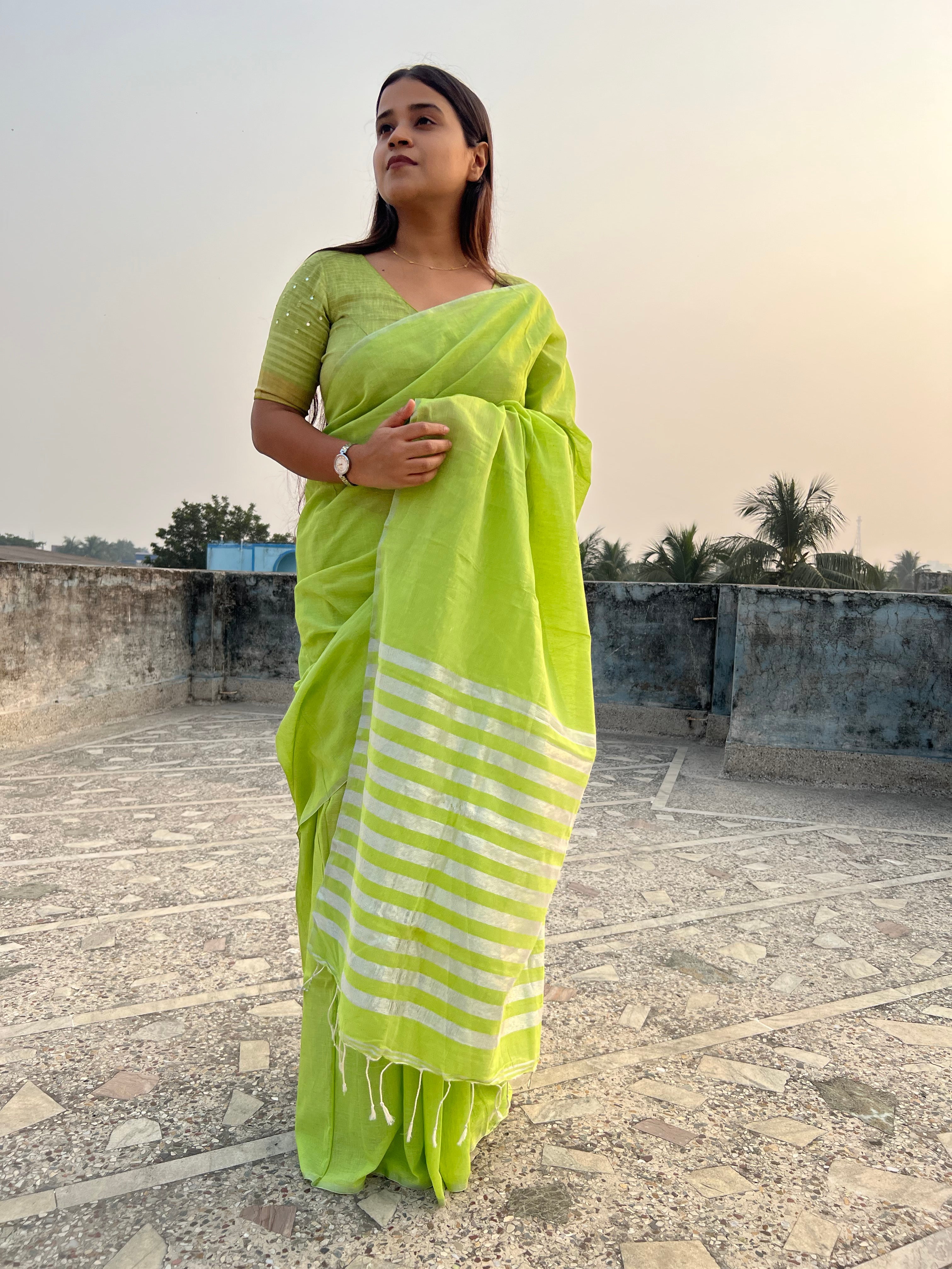 A woman standing on an open terrace wearing a green khaadi cotton saree with a silver-colored zari border and metallic stripe pattern.