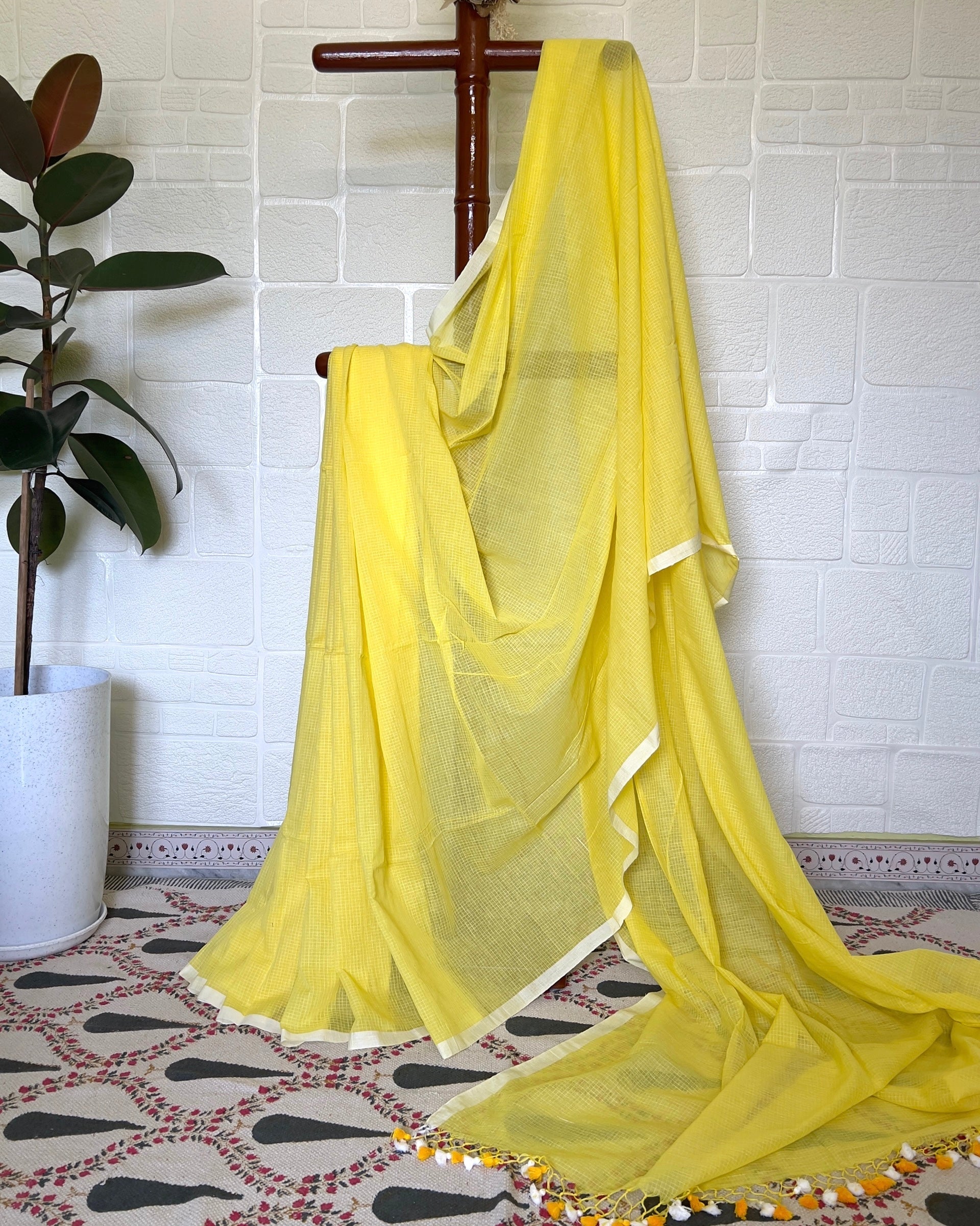 Yellow checkered handloom saree draped over a wooden rod against a white tiled wall.