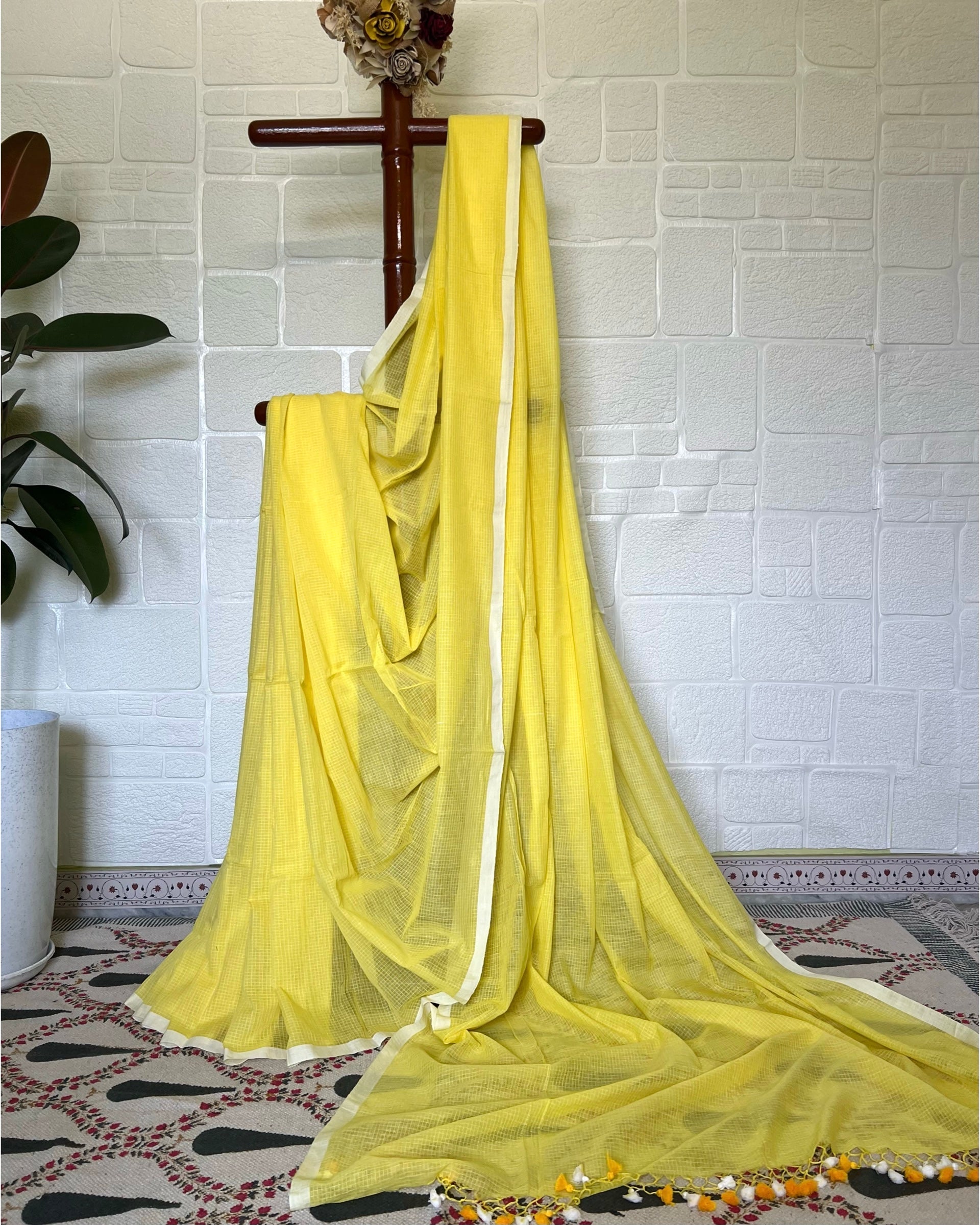 Yellow handloom Shopaame saree draped over a wooden rod against a white tiled wall.