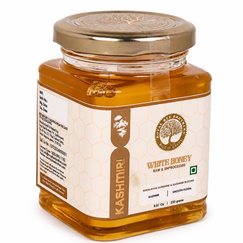 A glass jar of Kashmiri White Honey with a metallic gold lid and a cream-colored label featuring gold text and a honeycomb pattern, set against a plain white background.