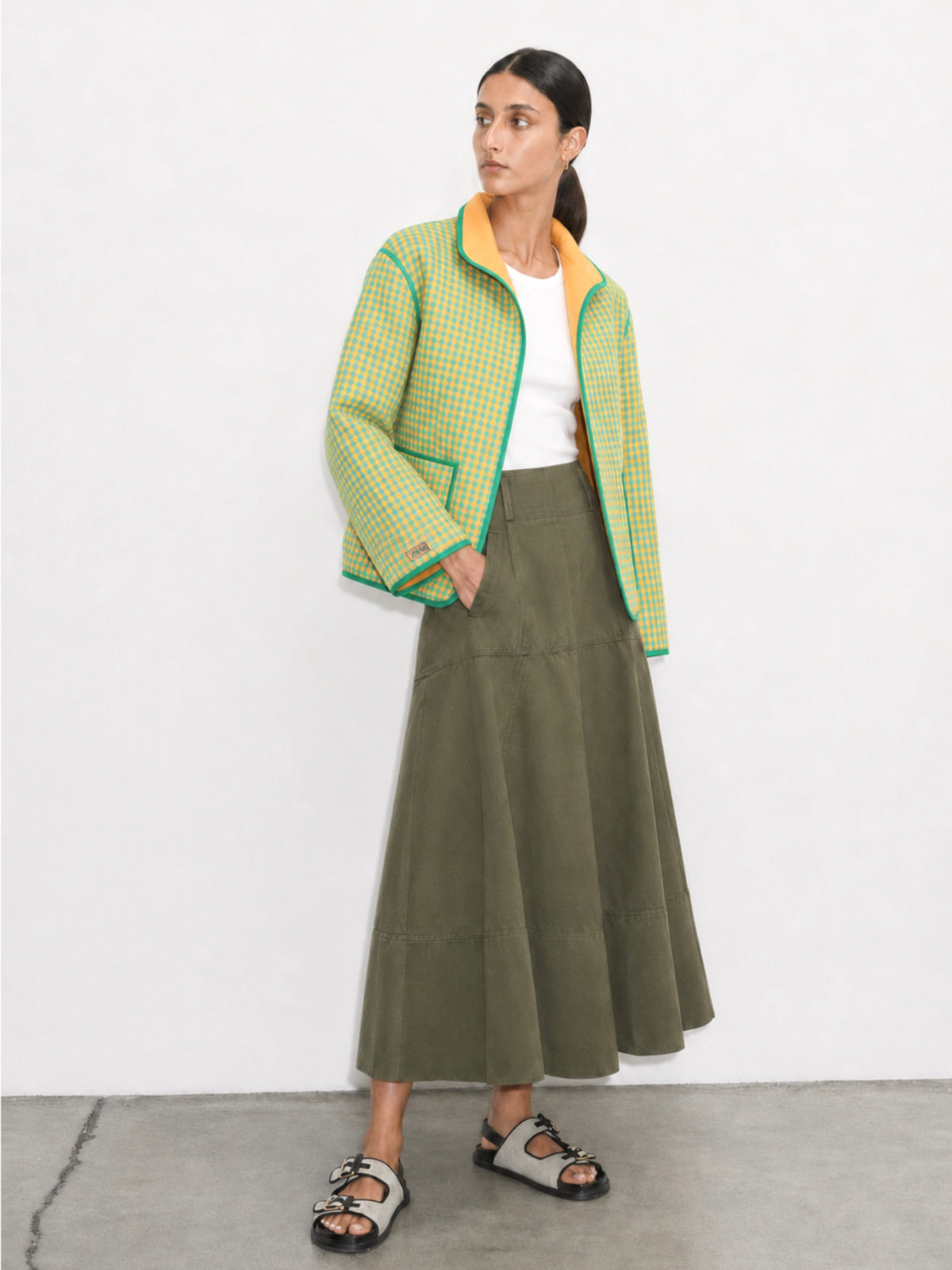 Woman wearing a green checkered jacket and olive green skirt on a white background