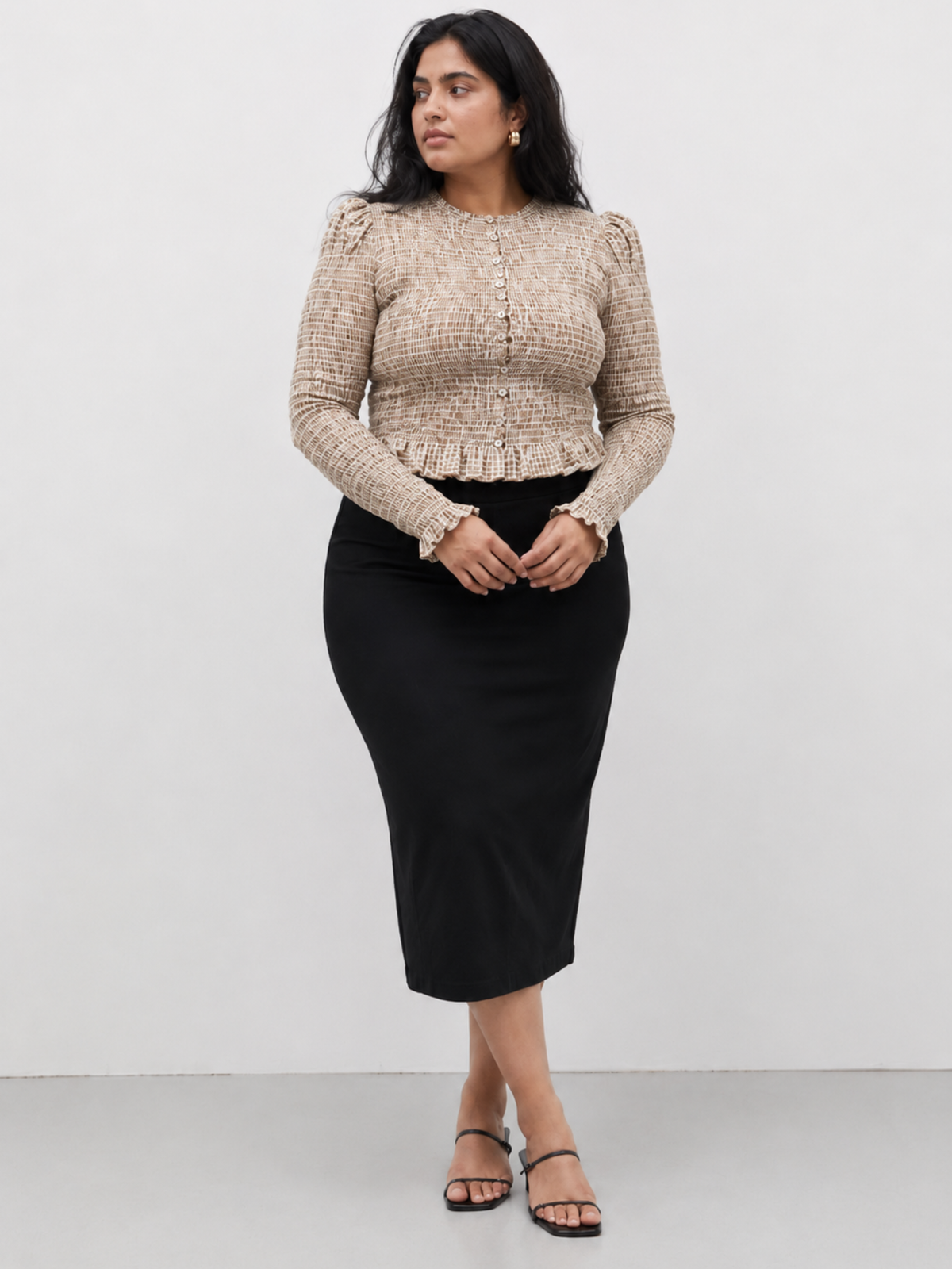 Woman wearing a brown and white checkered blouse with handcrafted smocking detail and black skirt against a white background