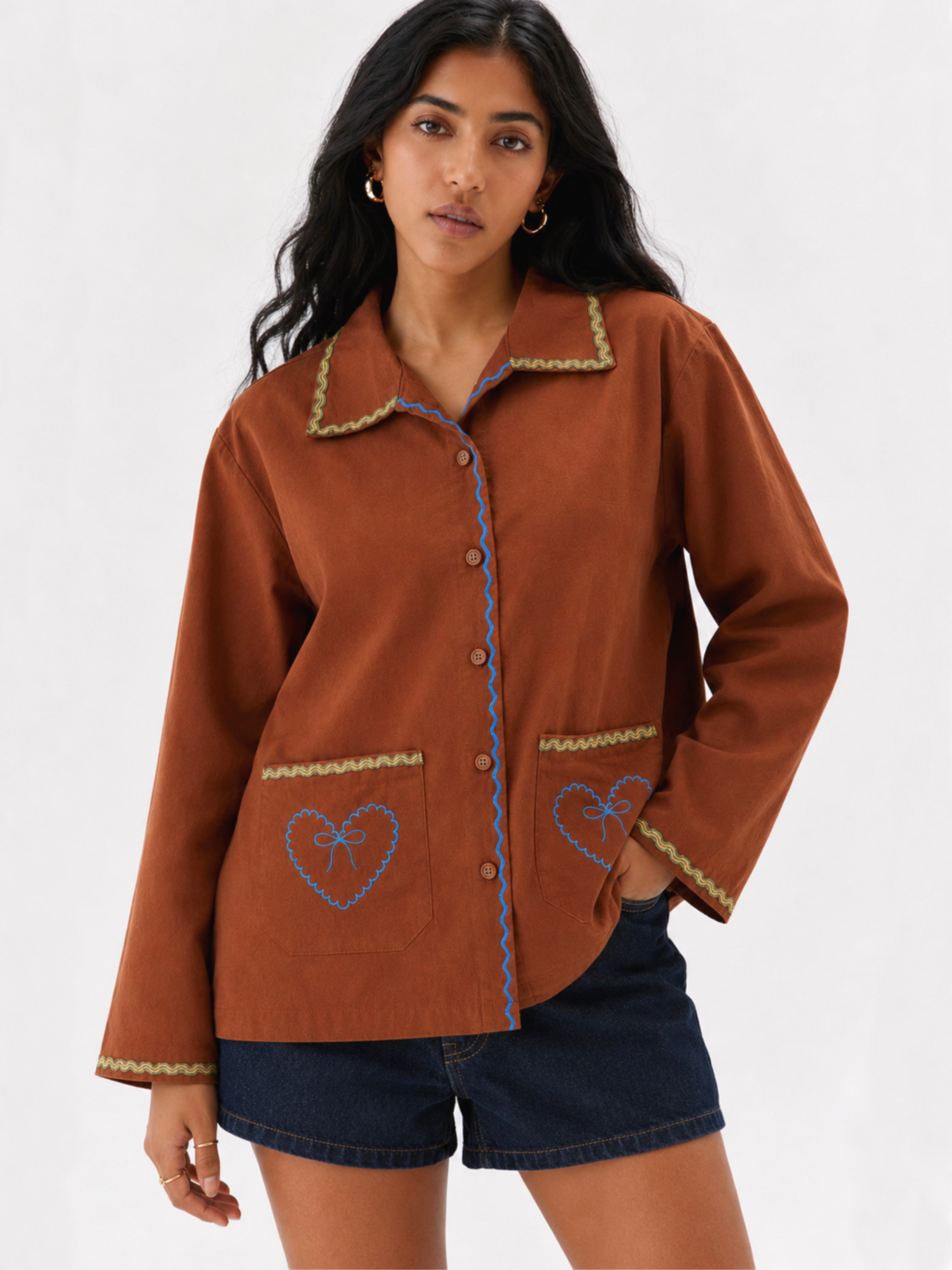 Woman wearing a brown cotton shirt with embroidered heart designs on a white background