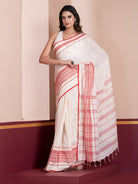 A woman modeling a white mulmul cotton saree with red geometric patterns and border details.