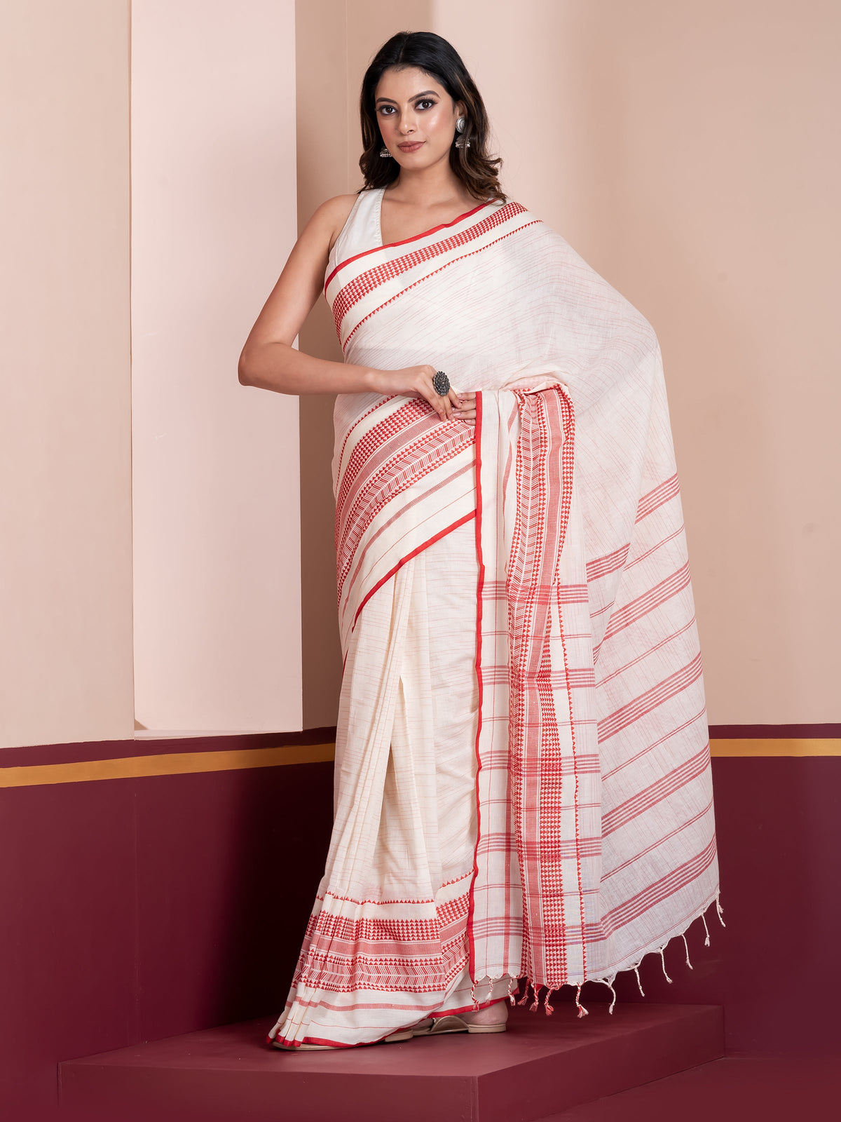 A woman modeling a white mulmul cotton saree with red geometric patterns and border details.