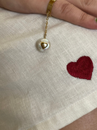 Hand with gold bracelet on white fabric with red heart embroidery