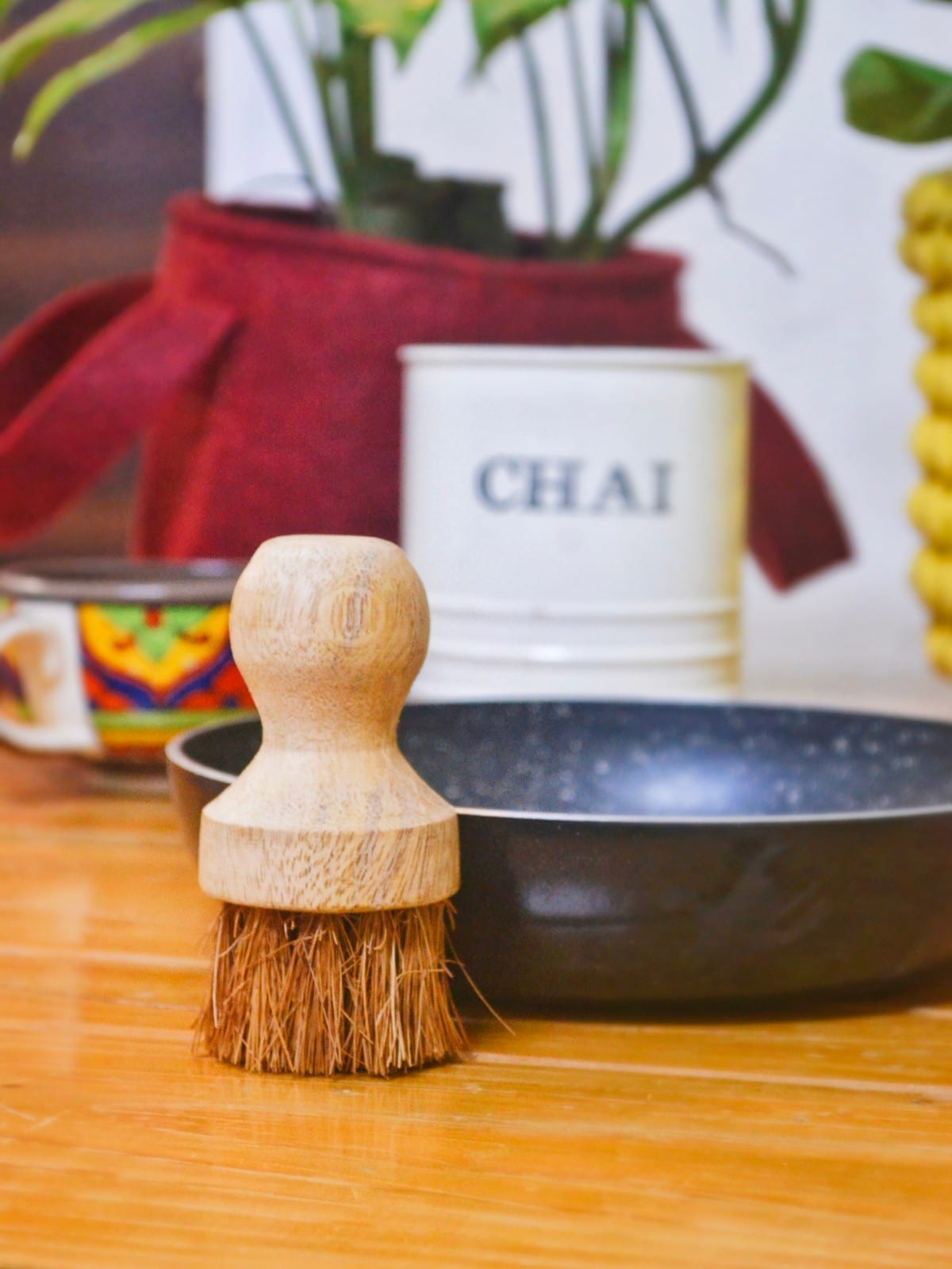 Almitra Sustainable wooden kitchen scrub brush with coconut fibre bristles placed beside cookware for eco-friendly dish cleaning.

