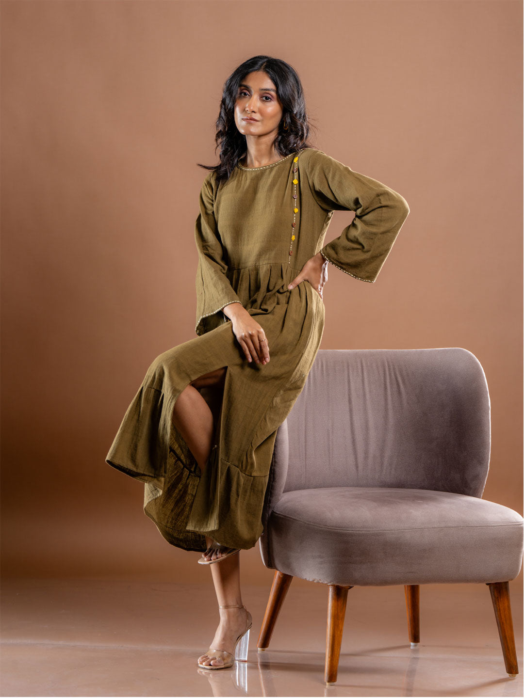 Side angle of olive green organic kala cotton midi dress for women featuring slit and embroidery detail with fluid bell sleeves.