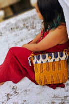 Young woman in a red dress with an Almitra Sustainables hand block printed sling bag in mustard yellow and cream, styled with bold Indian-inspired patterns and an artisan-crafted braided strap.