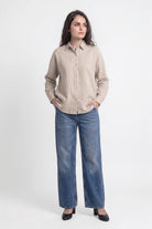A woman modeling a light beige linen button-up shirt and wide-leg blue jeans against a plain white studio background.