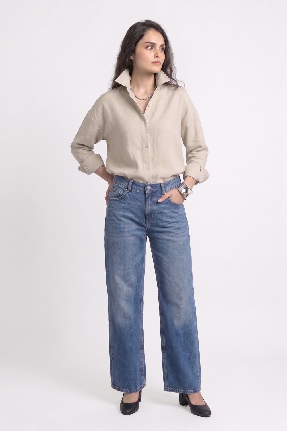 A woman modeling a beige long-sleeve button-up linen shirt and wide-leg blue jeans against a plain white studio background.