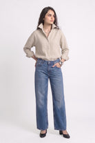 A woman modeling a beige long-sleeve button-up linen shirt and wide-leg blue jeans against a plain white studio background.