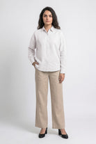A woman modeling a white long-sleeve linen button-up shirt and beige wide-leg linen trousers against a light gray studio background.