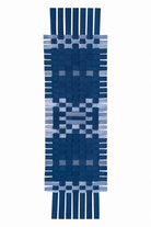 A woven rectangular textle with fringe ends, featuring a geometric pattern in shades of navy blue, medium blue, and light blue on a white background.