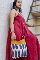 Model in a flowy red dress standing outdoors with a sustainable sling bag featuring a braided strap and blue-and-mustard ethnic print, designed by Almitra Sustainables for conscious everyday fashion.