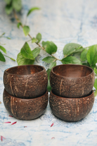 Stacked natural coconut shell bowls on a blue fabric with green leaves, ideal for eco-friendly dining and sustainable kitchens.