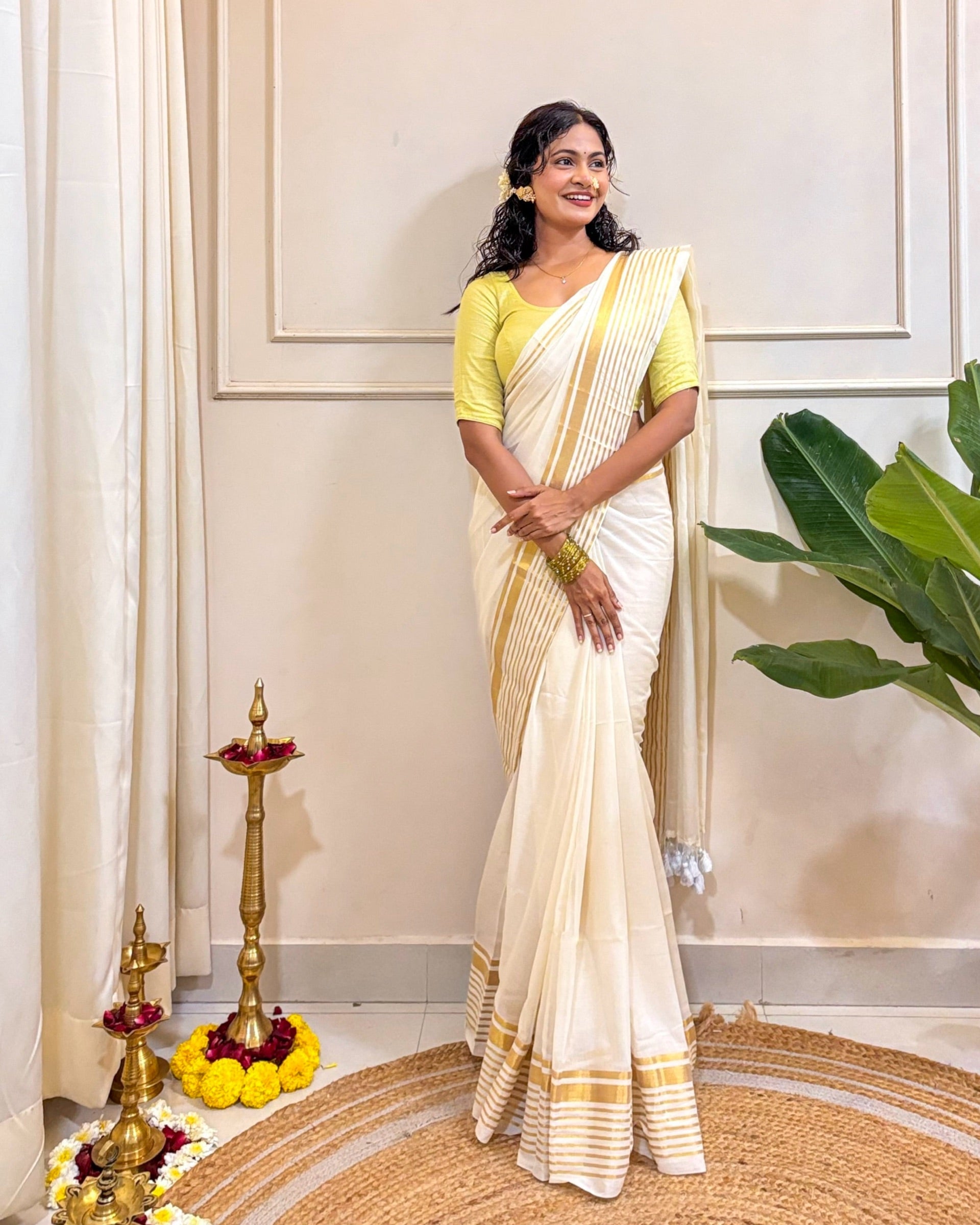 Woman in a white saree with yellow blouse standing indoors with decorative elements.