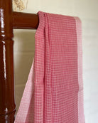 Pink checkered handloom cotton Shopaame saree draped over a wooden chair against a white wall.