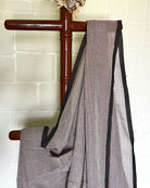 Brown checkered handloom saree by Shopaame draped over a wooden rod against a white brick wall.
