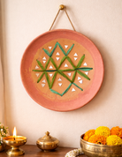 Decorative wall plate with geometric design on a wall with candles and flowers below.