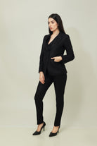 A woman models a tailored black linen blazer with a matching buttoned waistcoat and slim trousers, styled with black pointed heels against a soft neutral studio backdrop. The look is sleek, structured, and contemporary.