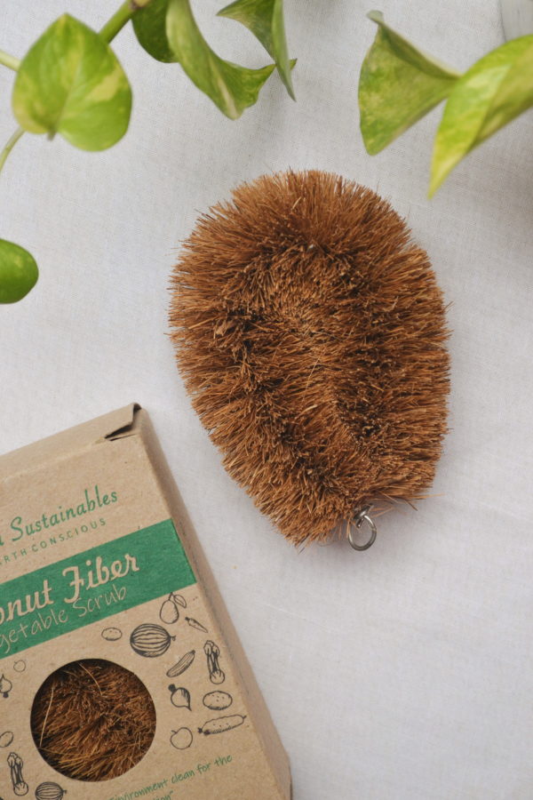 Top view of a natural coconut fiber vegetable scrub brush with a sturdy coir bristle texture, displayed beside its eco-friendly kraft packaging on a white background, perfect for sustainable kitchen cleaning, by Almitra Sustainables.