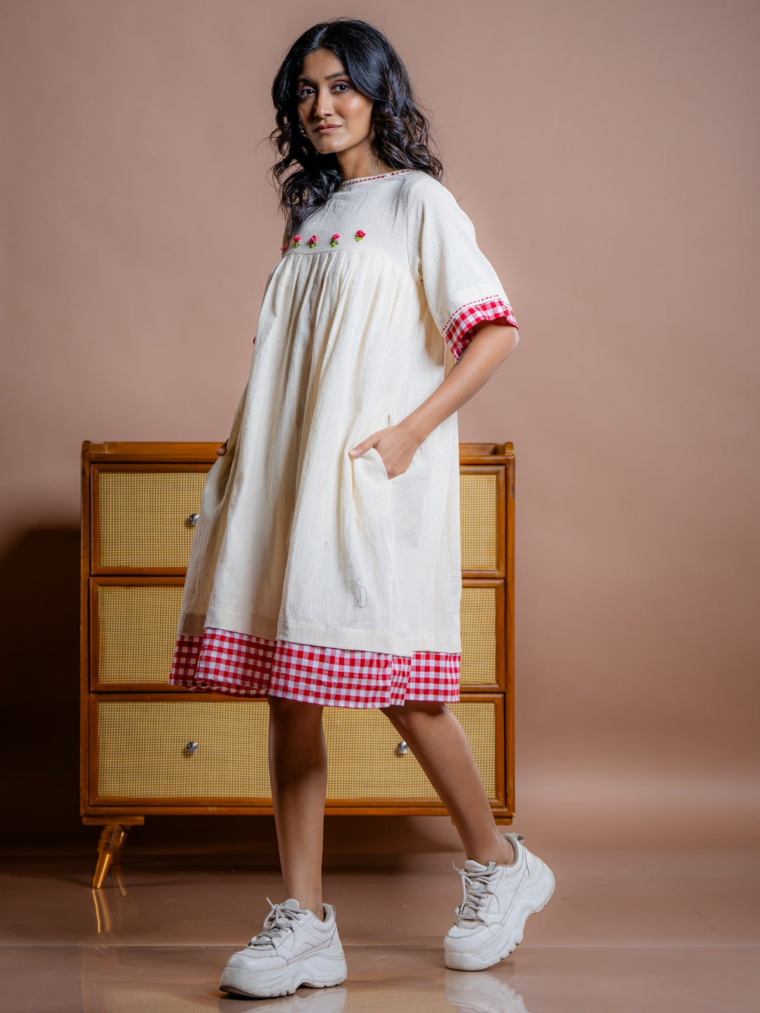 Off-white handwoven kala cotton knee length dress with red details at hem and hand embroidery. Best sustainable dresses brands in India.