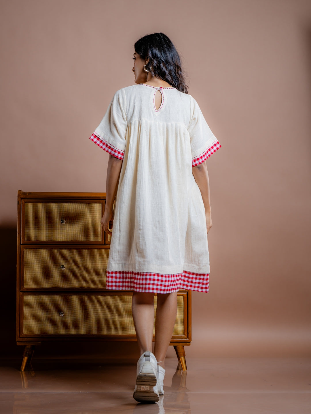 Women wearing off-white handwoven kala cotton tunic dress with red trims. adorn with hand embroidery, this dress features half sleeves, gathered yoke and two roomy pockets. Stylish, sustainable and made to be lived in.