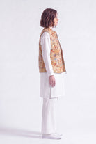 A woman shown in profile wearing a white traditional outfit with a sleeveless patterned  linen vest, photographed against a clean white studio background.