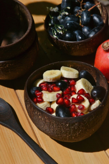 Sustainable coconut bowl filled with banana, pomegranate, and grapes, perfect for smoothies and fresh fruit servings.