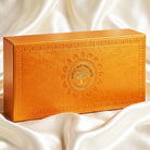 An ornate rectangular golden-orange box with embossed decorative borders and a central Royal Bee Bronzes logo, resting on draped white satin fabric.