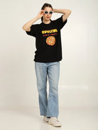 Person wearing a black t-shirt with a graphic design and text, light blue jeans, and white sneakers on a plain background.