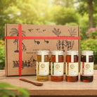 Four jars of honey with a decorative box on a wooden table outdoors.