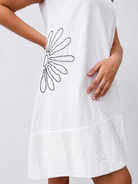 A white sleeveless dress with a black beaded daisy design on the side pocket and a textured horizontal pintuck detailing near the hem, shown on a model against a light gray background.