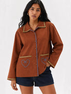 Woman wearing a brown cotton shirt with embroidered heart designs on a white background